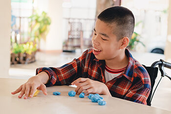 Disabled child in wheelchair moulding clay at the table.